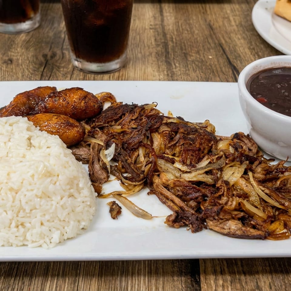 Plated meal featuring white rice, roasted potatoes, crispy fried onions, dark beans, and sandwiches on a wooden table.